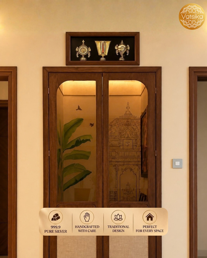 A traditional wooden double door Pooja room with glass panels, featuring Silver Shanku Chakra Nama on top of the Door, shown installed in a beige wall. The door features an etched illustration of a temple and a plant motif on one pane.